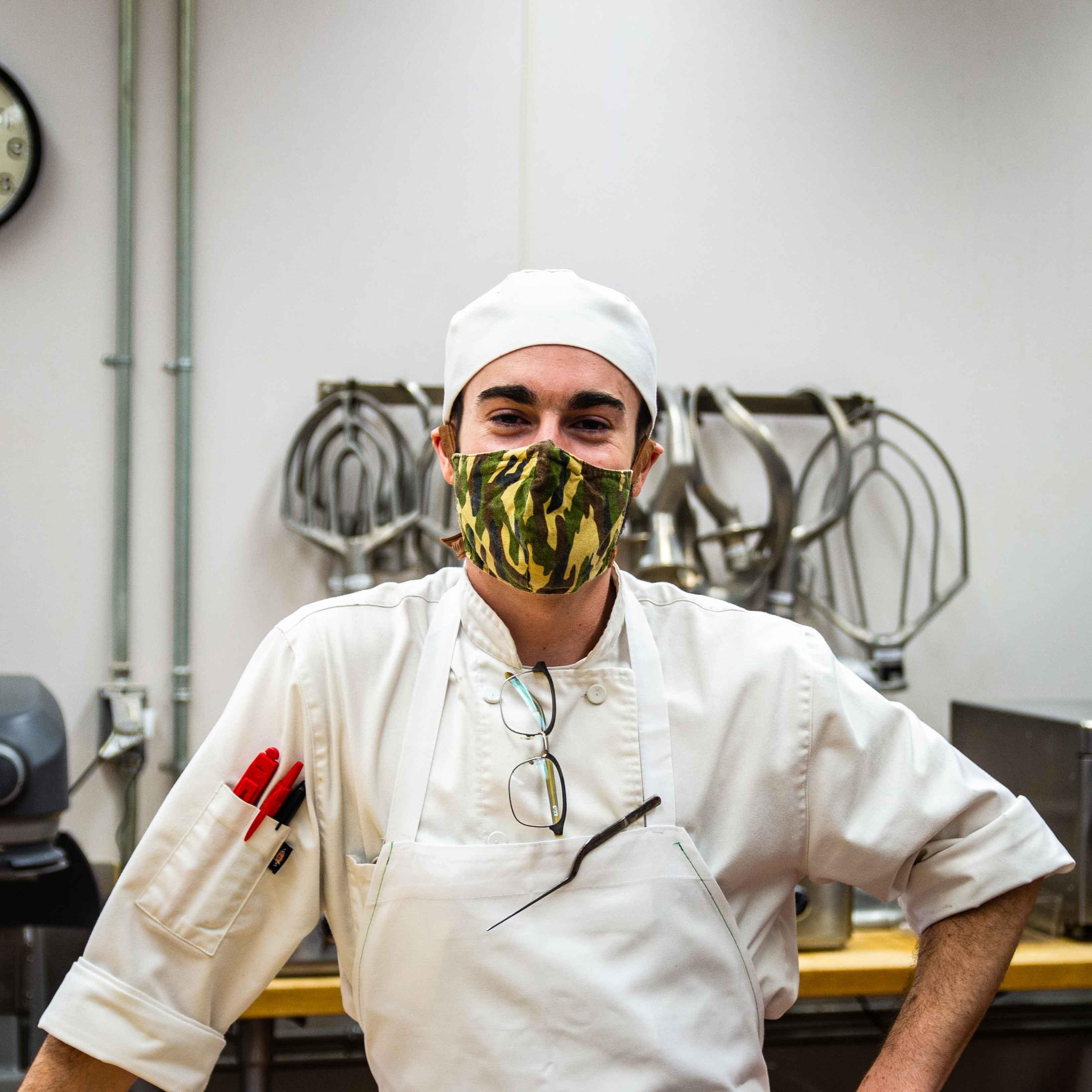 Student in white chef's clothes and masks poses in kitchen